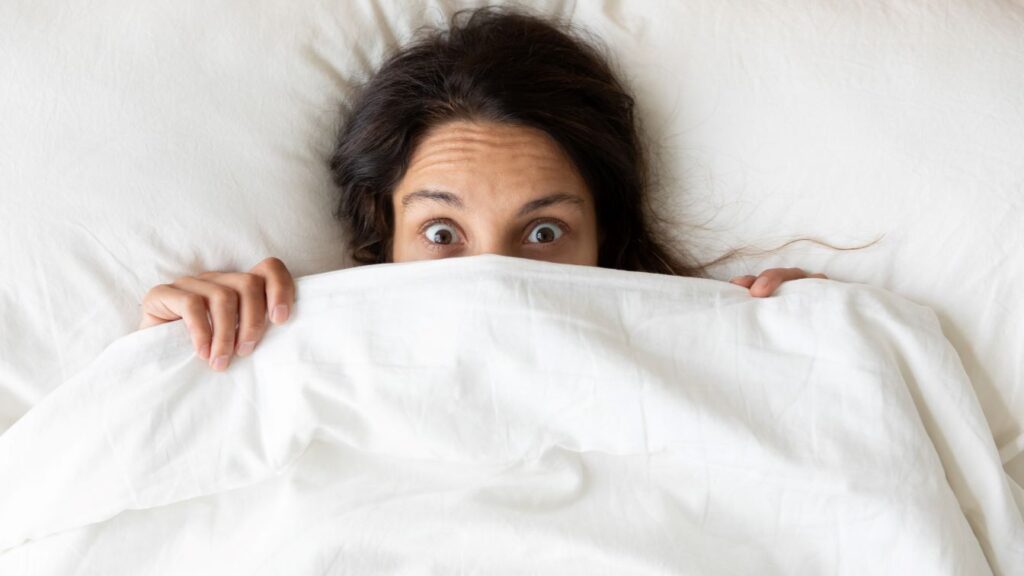 A woman hiding under bed sheets.